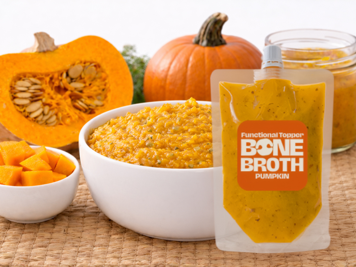 Wunderdog Pumpkin Bone Broth functional topper pouch beside a bowl of pumpkin puree with fresh pumpkin, seeds, and herbs on a woven mat background.